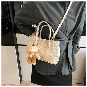 Detail of beige woven bucket bag with cute plush bear charm and adjustable strap
