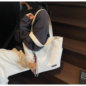 Detail of off-white canvas tote bag with brown plush bear charm and woven cord on wood stairs