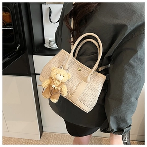 Detail of beige woven texture tote bag with a cute plush bear charm and golden hardware