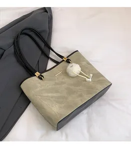 Detail of grey-green tote bag with gold metal trim and fluffy pompom charm on a blazer