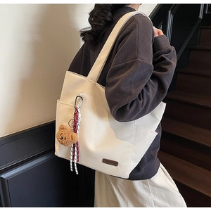 Detail of white canvas tote bag with brown logo plate and a cute teddy bear charm