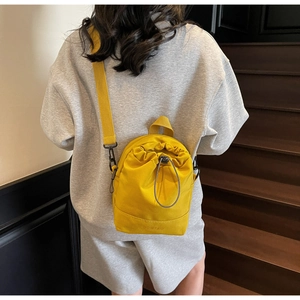 Detail of a bright yellow drawstring bucket bag with branded strap and canvas texture