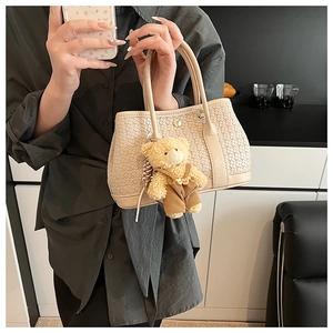 Detail of beige woven tote bag with cute brown bear charm and metal magnetic closure