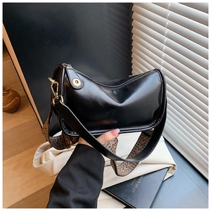 Détail du sac en cuir noir brillant avec une large bandoulière tissée géométrique