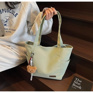 Detailed side view of light green canvas tote bag featuring practical pocket and bear charm
