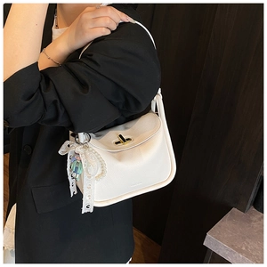 Detail of white litchi leather pillow bag with pearl bow charm and gold lock hardware
