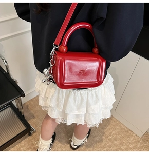 Vue détaillée du sac bandoulière en cuir ciré rouge avec gaufrage de lettres et breloque