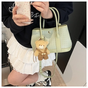 Detail of light green woven bucket bag with a cute teddy bear charm and cross-pattern texture