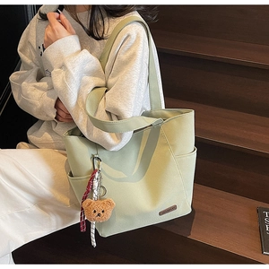Detail of green canvas tote bag with bear charm and brand label on wooden stairs