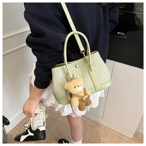 Detail of light green woven bucket bag with teddy bear charm and metal buckle closure