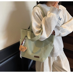 Close-up of light green canvas tote bag featuring brown leather logo and cute bear charm