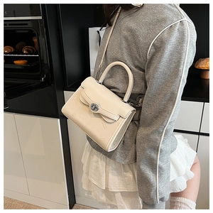 Detail view of cream crossbody bag featuring embossed patterns and round top handle