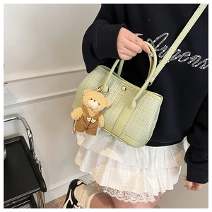Detail view of light green woven texture bucket bag featuring a cute teddy bear charm
