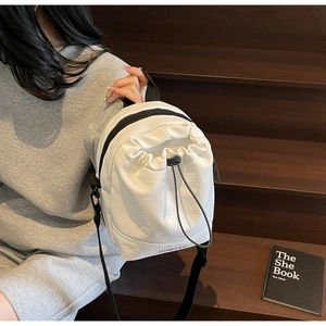 Detailed view of white drawstring nylon shoulder bag with adjustable black strap and brand logo