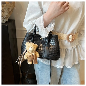 Detail of black woven texture handbag with a cute brown plush bear charm accessory