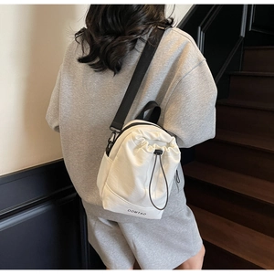Detail showing the adjustable black shoulder strap and drawstring closure of the white bag