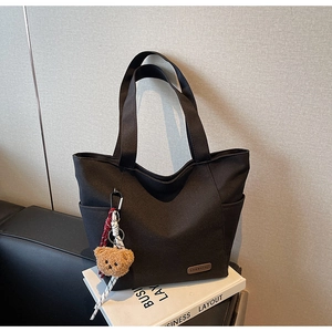 Detail of black canvas tote bag showing SHANHEYC leather label and cute bear charm