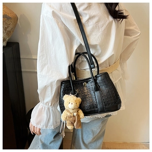 Detail view of black woven texture handbag with gold snap and cute brown bear charm