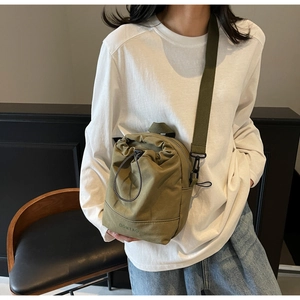 Olive green canvas drawstring crossbody bag shown as worn by a model in casual style