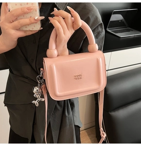 Détail du sac à main rose avec poignée ronde, logo de la marque et breloque chien ballon
