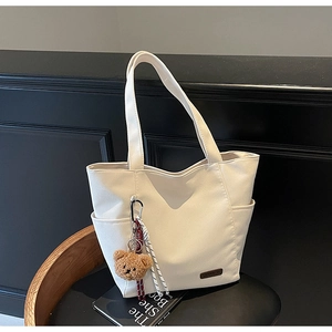 Detail of minimalist cream canvas tote bag with brown bear charm on wooden stool