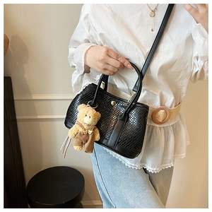 Detail of black woven texture handbag with golden buckle and a cute bear bag charm