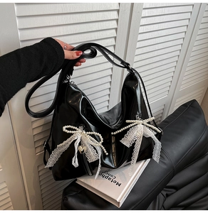 Detail of black patent leather tote bag featuring lace bows and pearl chain accents