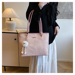 Pink faux suede tote bag detail featuring metal logo and a cute white furry pom-pom charm