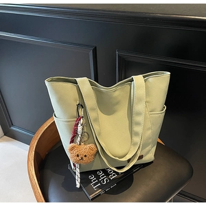 Close-up of light green canvas tote bag with a small plush bear charm on a black chair