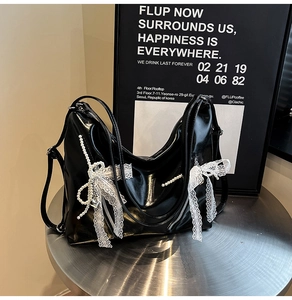 Close-up of black glossy tote bag featuring lace bow, pearls, and metallic heart charm