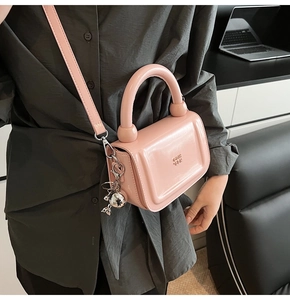 Sac à main rose en cuir verni avec breloque sphérique porté par une personne