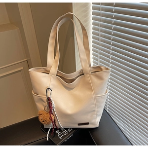 Detail of beige tote bag with cute bear charm and side pockets on a minimal background