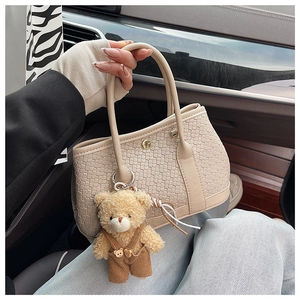Detailed view of beige woven texture handbag with golden buckle and cute plush bear charm