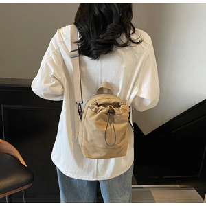 Detail of khaki canvas drawstring bucket bag featuring a wide adjustable shoulder strap