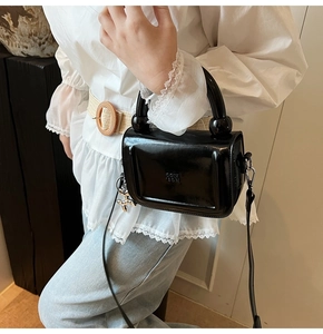 Détail du mini sac en cuir verni noir avec poignée ronde et breloque chiot argentée