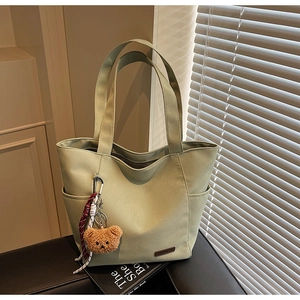 Detail of light green canvas tote bag with brown plush bear charm and woven cord detail