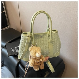Detail of light green woven bucket bag featuring a cute brown plush bear charm