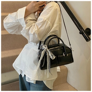 Chic black patent leather bow shoulder bag shown with minimalist casual outfit on stairs