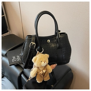 Detail of black woven texture handbag with golden buckle and cute plush bear charm