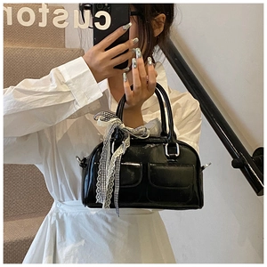 Détail du sac Boston en cuir verni noir avec doubles poches et nœud en dentelle