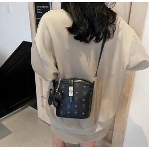 Classic black bucket bag with textured pattern and decorative charm worn by model