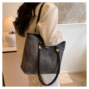 Detail of dark grey tote bag with textured finish, gold buckles, and black shoulder straps