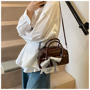 Détail d'un sac Boston marron foncé avec un nœud en dentelle blanche et une finition mate