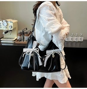 Detail of black patent leather tote bag with lace bow, pearls, and heart pendant detail