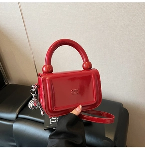 Détail du mini sac à main en cuir verni rouge avec poignée et breloque en métal argenté