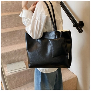 Detail view of large black leather tote bag with long handles and a matching pouch
