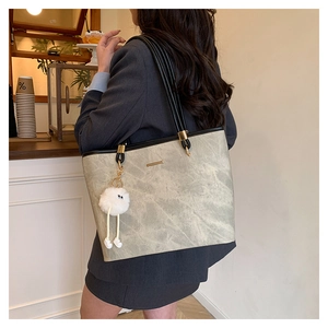 Detail view of a large grey tote bag with stone texture, black straps, and a white fur charm