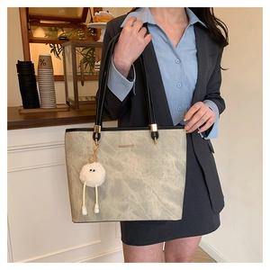 Gray tote bag detail with marble texture and white plush ball charm on black strap