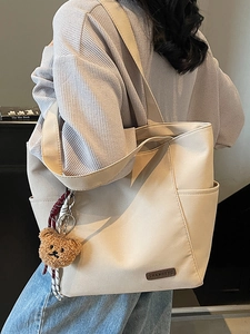 Minimalist beige tote bag with a brown bear pendant shown on model for casual commuting style