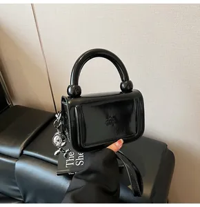 Détail du sac à main en cuir verni noir avec fermoir rond et breloque chien argentée